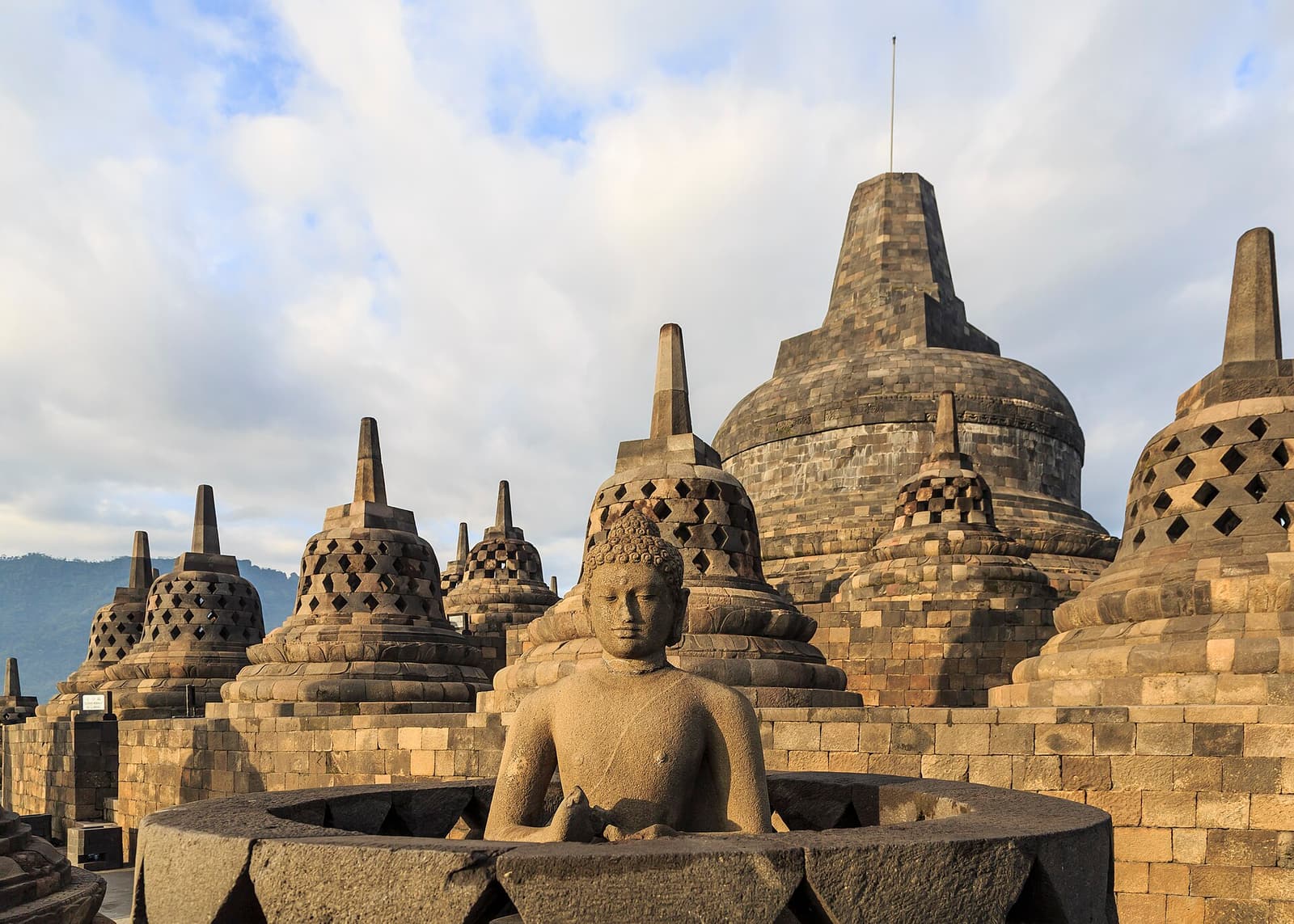 Bell-shaped stupas and a seated Buddha on the upper terraces of Borobudur