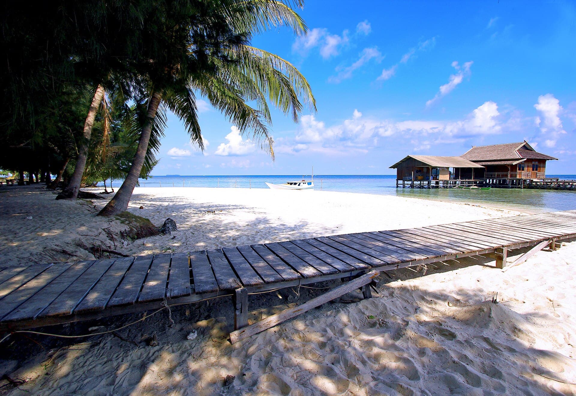 A wooden jetty leading to a stilt hut on a white-sand beach in the Karimunjawa Islands