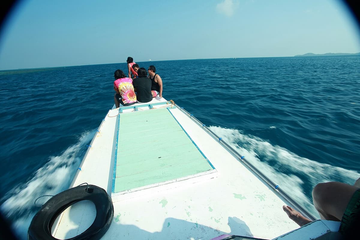 Passengers sitting on the bow of a tour boat crossing deep blue water in Karimunjawa